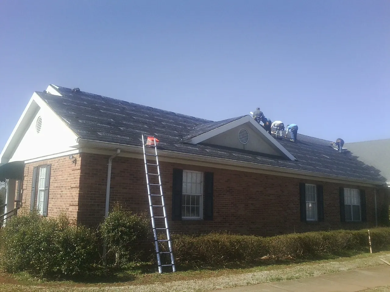 Crew tearing shingles off a brick ranch roof with a ladder set — Metal Roof Repair work by our crew in Union Grove