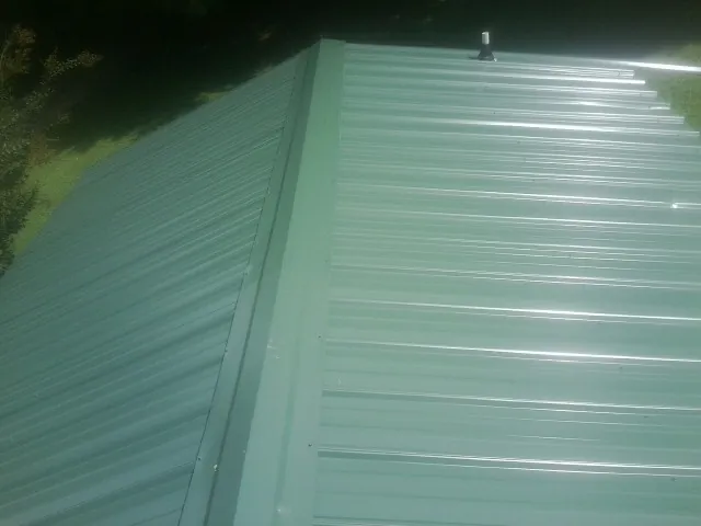 New green metal panels meeting at the ridge of a roof — Flat Roof Repair work by our crew in Union Grove