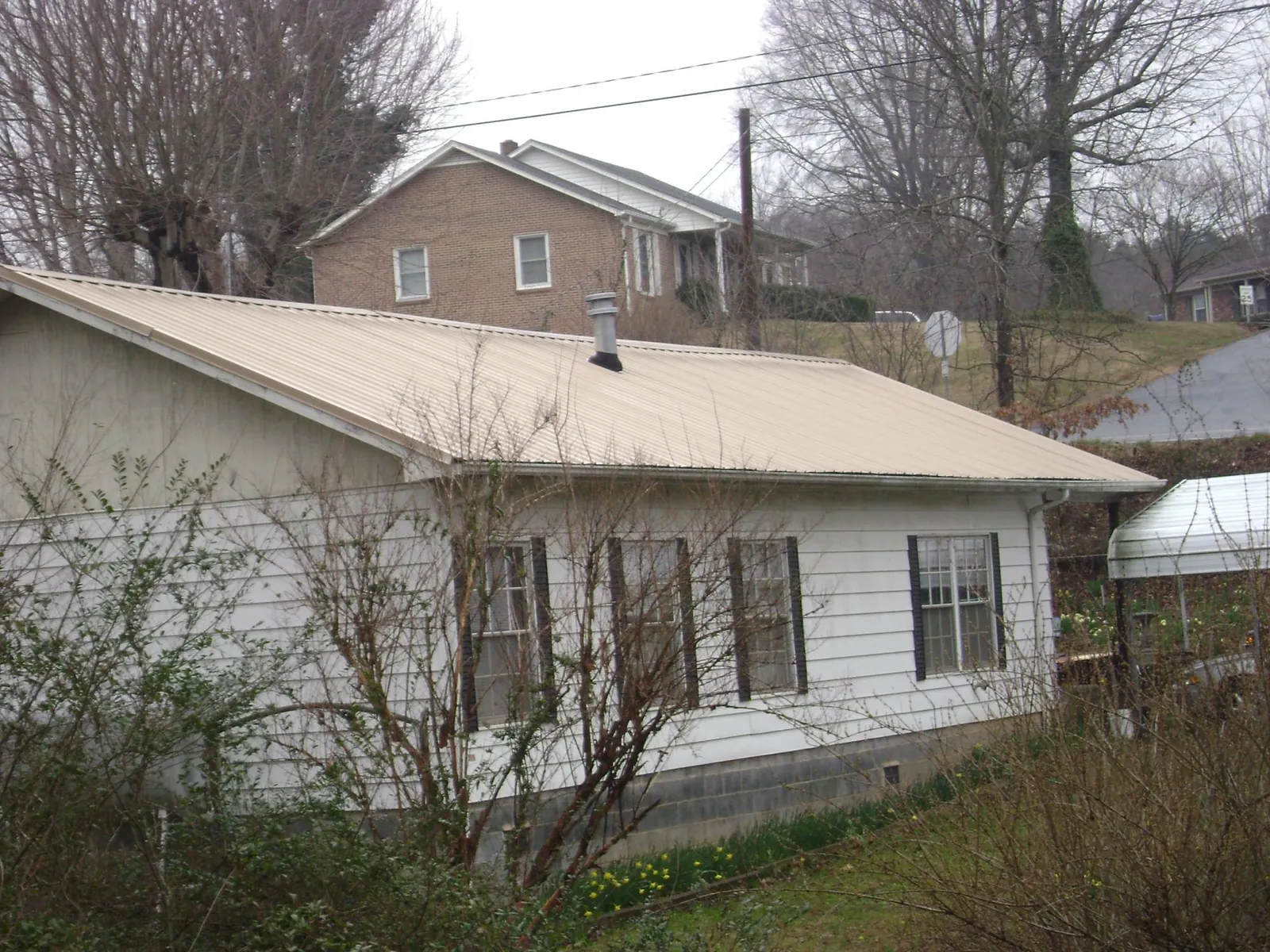 Tan metal roof on a white sided house set into a hillside — Commercial Roofing by Roofing Brothers in Union Grove